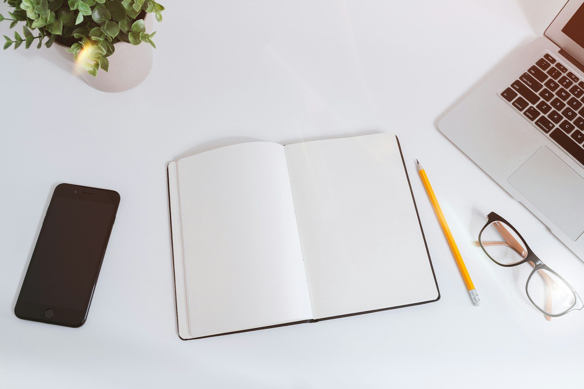 Smartphone, open notebook and glasses on a white desk