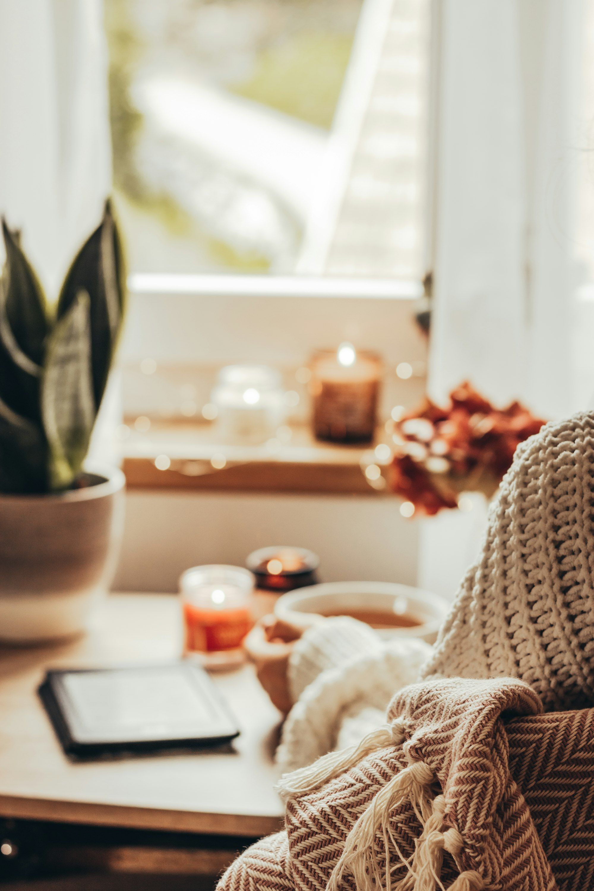 Person in a knit sweater holding a warm drink beside candles