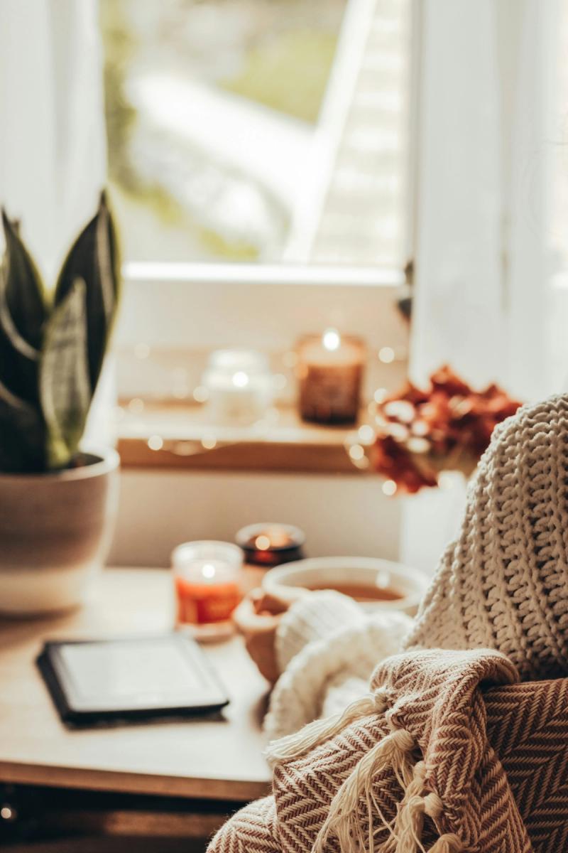 Person in a knit sweater holding a warm drink beside candles