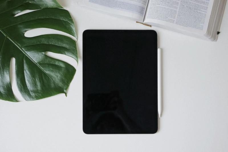Smartphone with the screen off lying beside an open book on a white desk