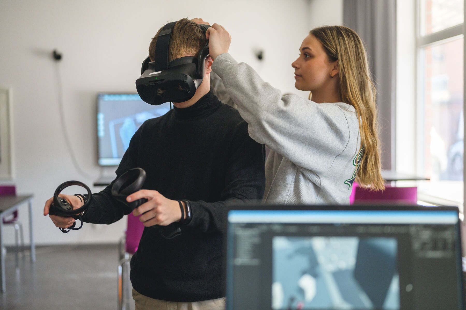 Elev skriver kod på en dator medan två elever använder VR-set i bakgrunden.