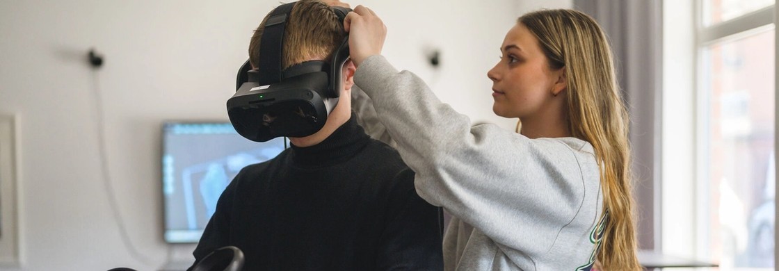 Elev skriver kod på en dator medan två elever använder VR-set i bakgrunden.