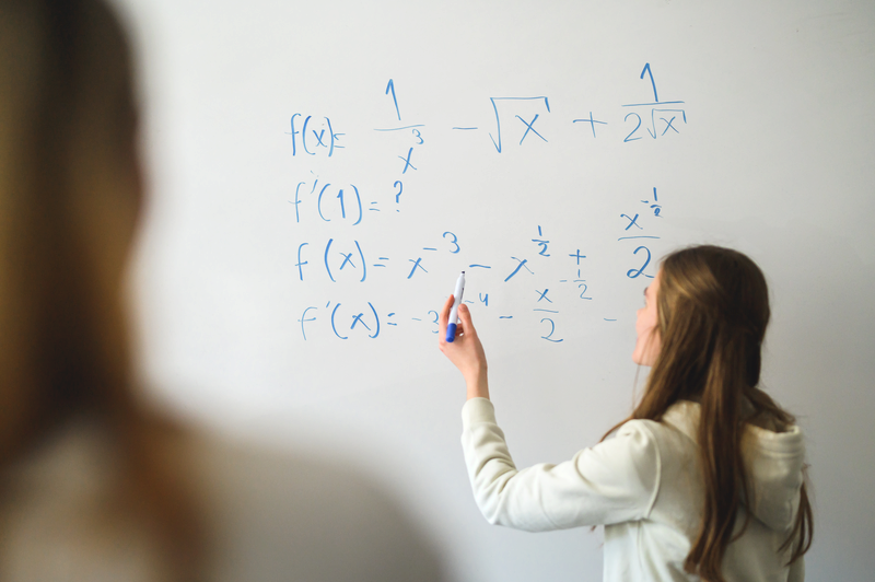 En elev står framför en whiteboard och skriver ekvationer på tavlan.