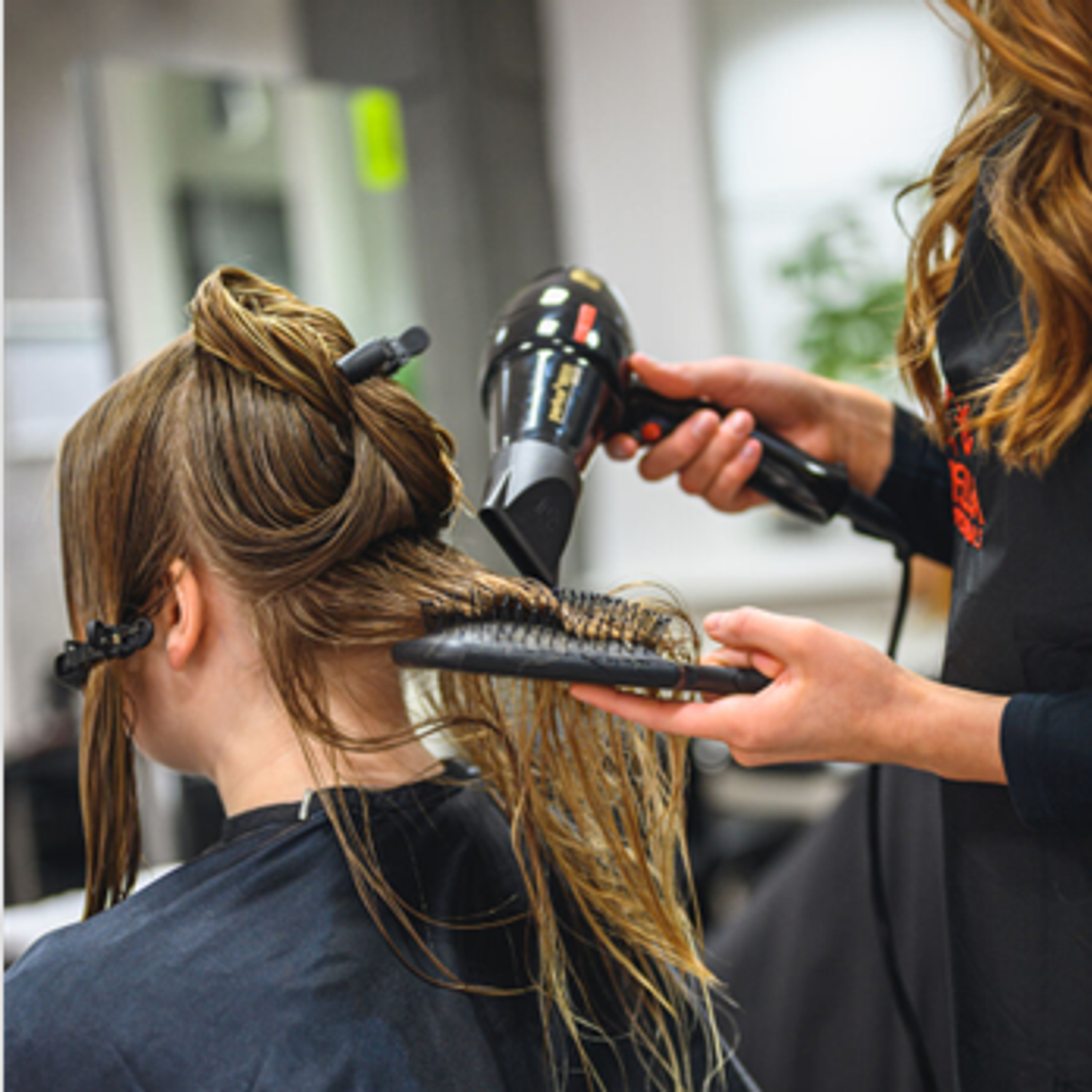 Frisörelev fönar hår på kund