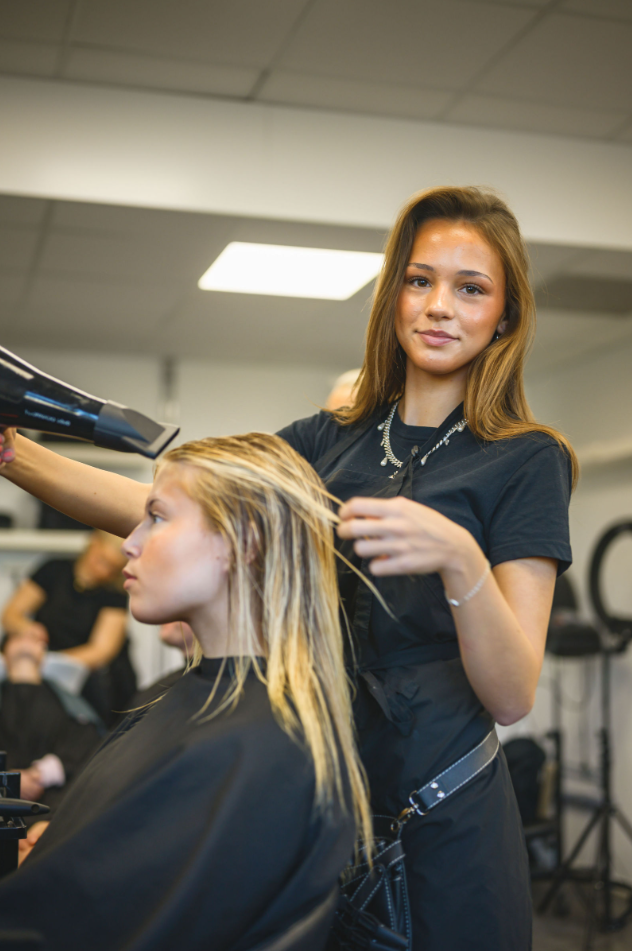 Elev fönar hår på kund