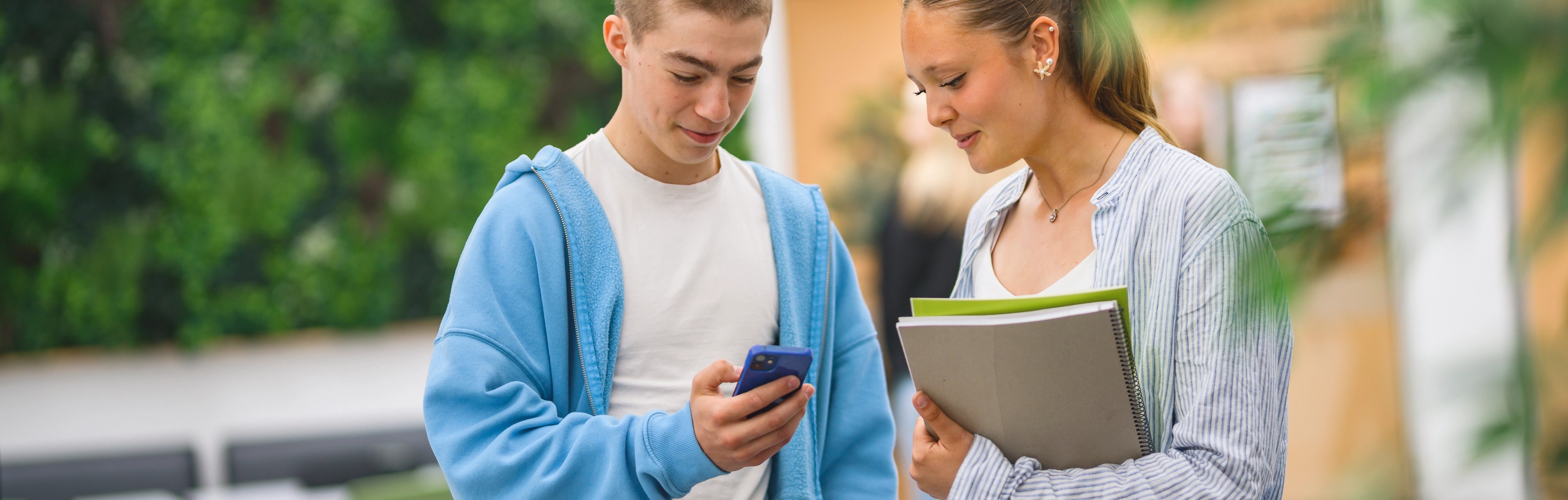 två elever står och tittar i telefon