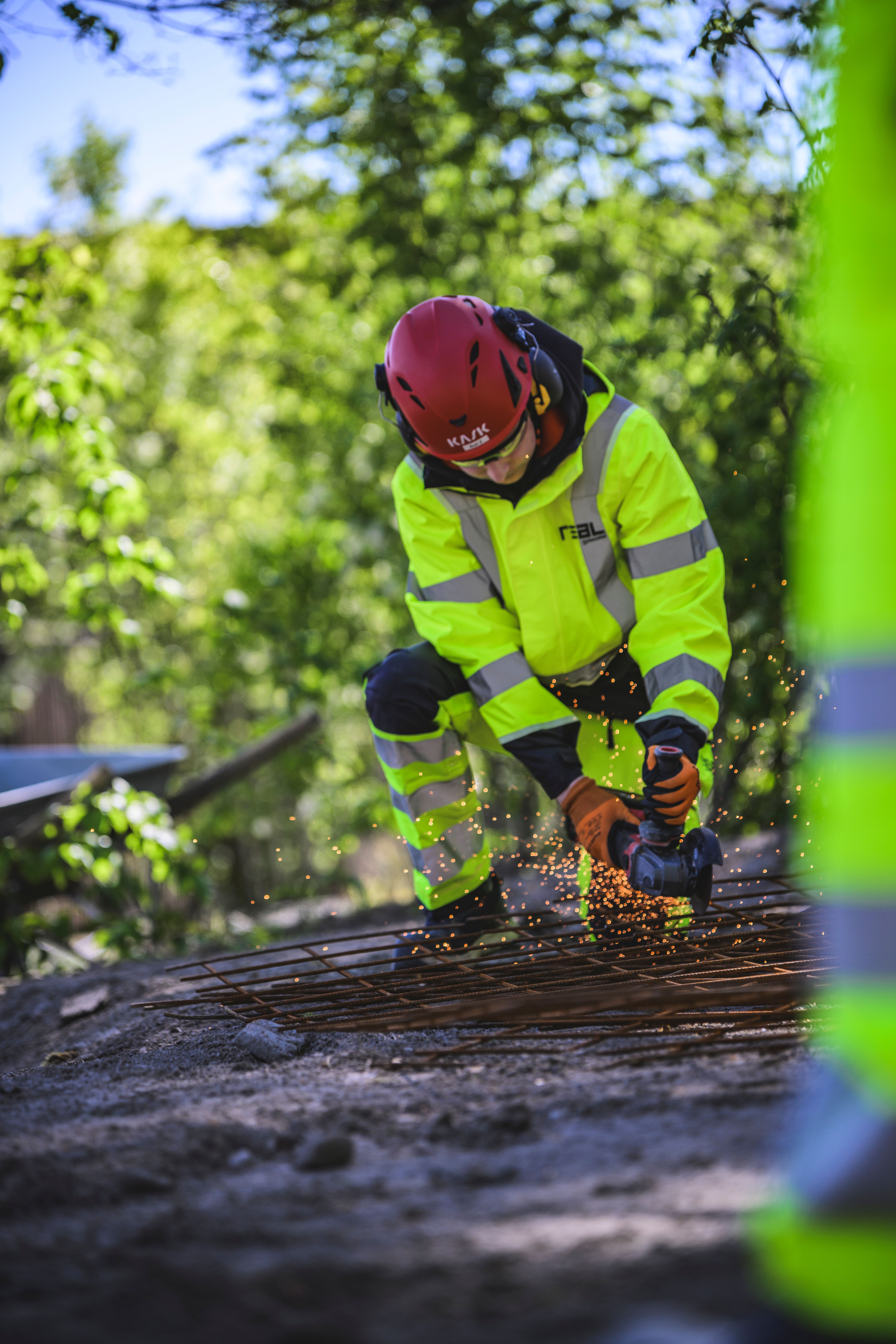 En elev i varselklädsel använder en vinkelslip på ett galler.