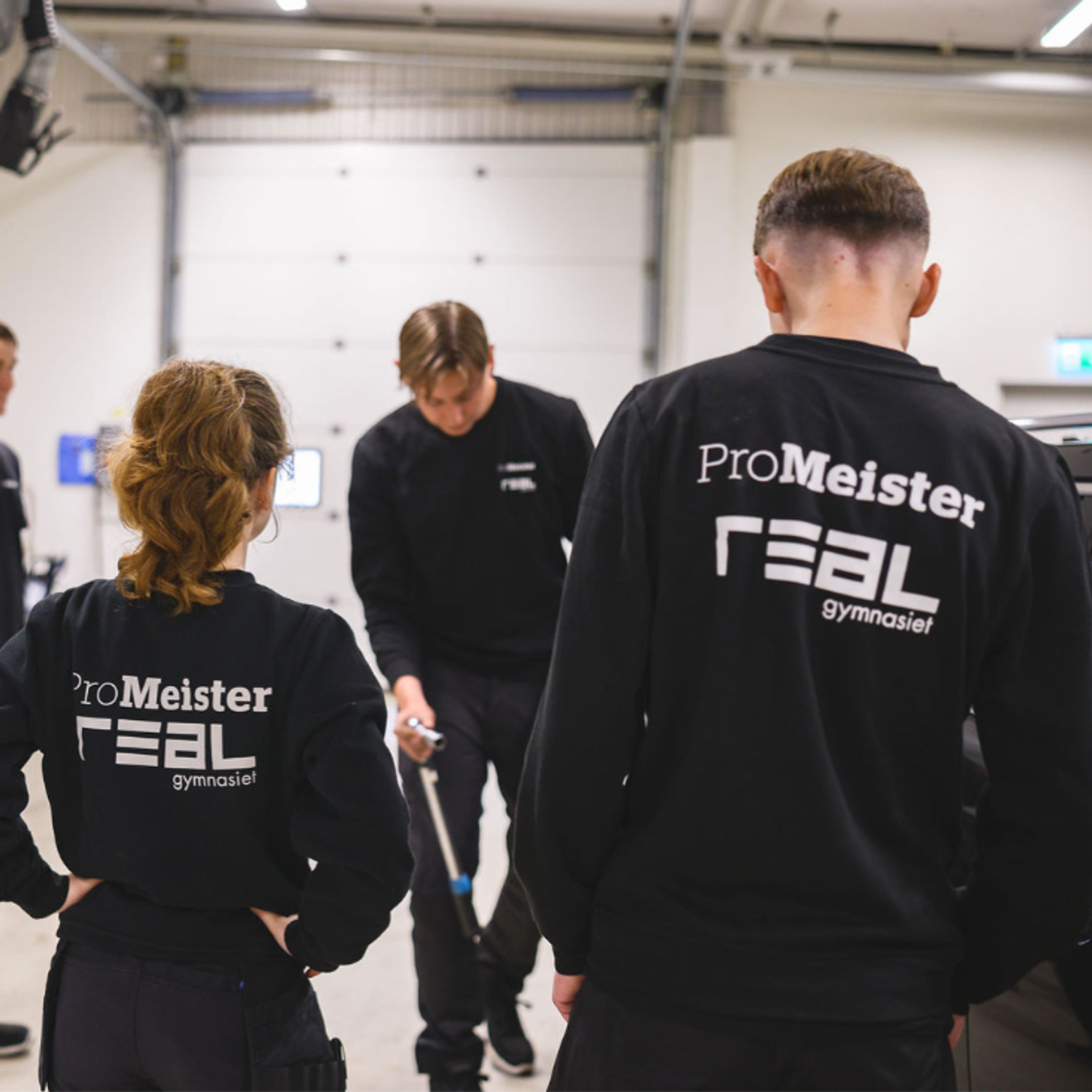 ryggar på elever med realgymnasiets logga plus promeisters logga på tröjan