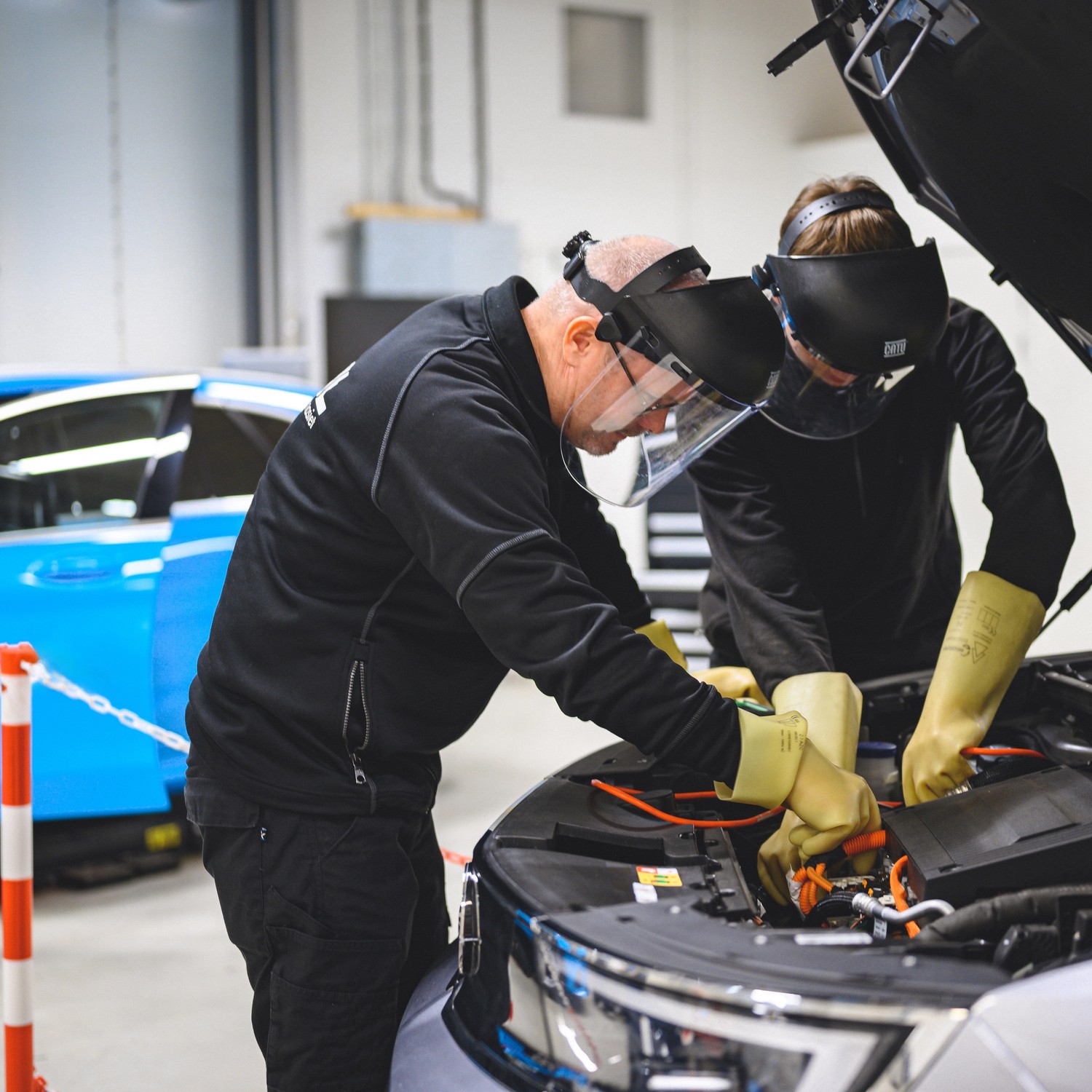 Elev med handledare arbetar i motorn på bil i verkstad.