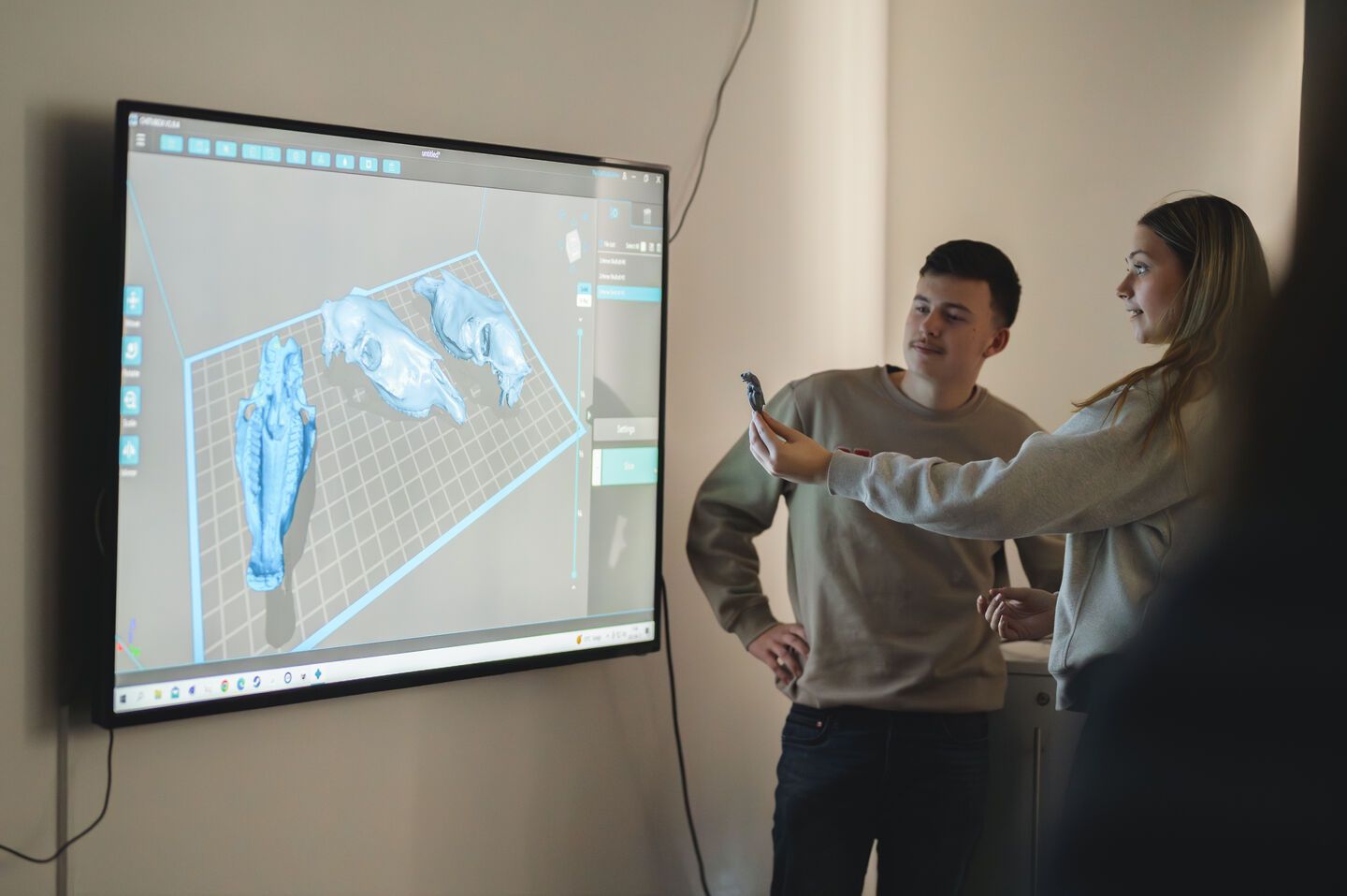 Två elever står framför en stor skärm som visar deras 3D-modeller.