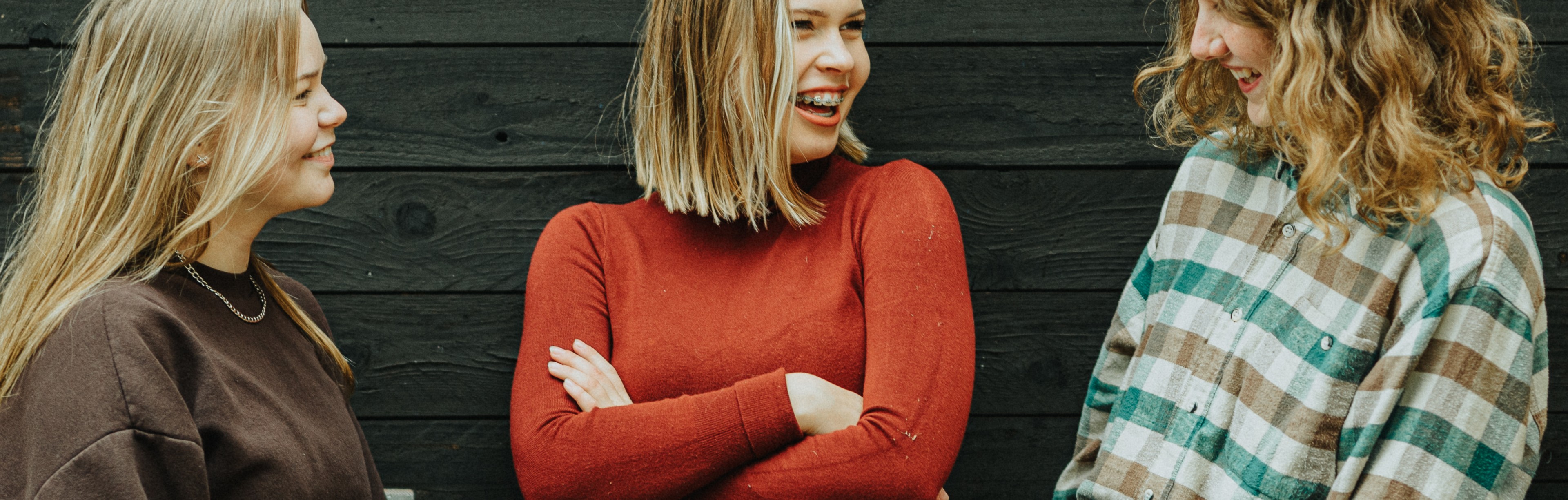 Tre tjejer står och pratar och ler vid mörk vägg