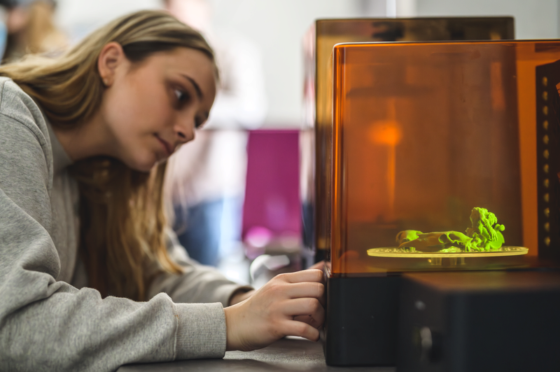 En glad elev med hjälm och skidglasögon bär sina skidor över axeln i solsken på fjället.