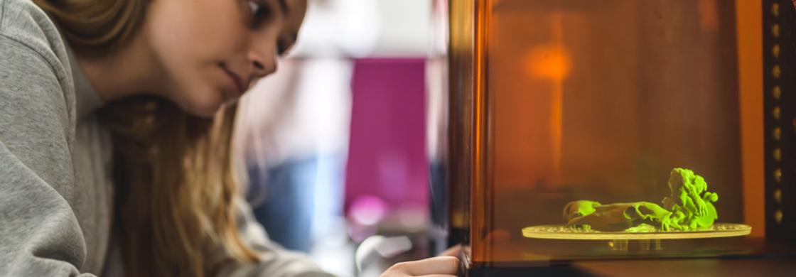 En glad elev med hjälm och skidglasögon bär sina skidor över axeln i solsken på fjället.