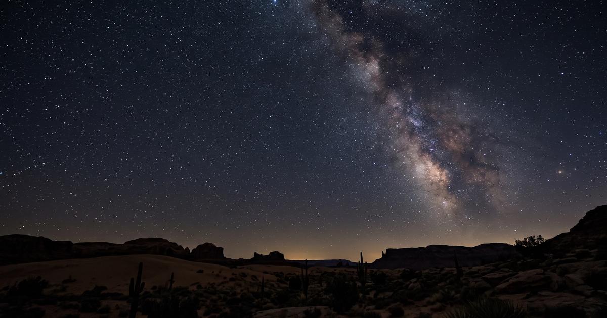 The Milky Way stretching across a dark night sky above a quiet desert horizon.