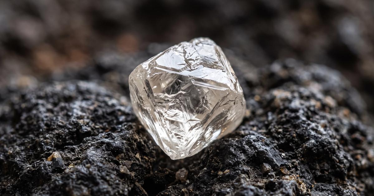A raw uncut diamond crystal resting on dark stone.