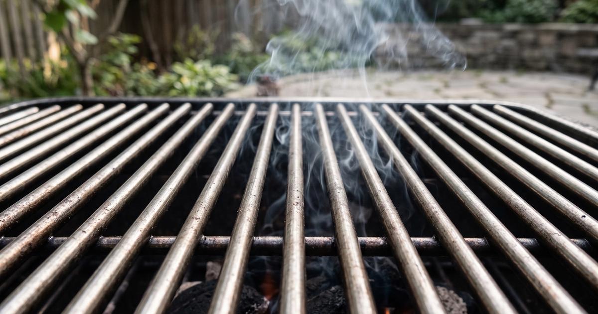 A clean stainless steel grill grate with steam rising in daylight.