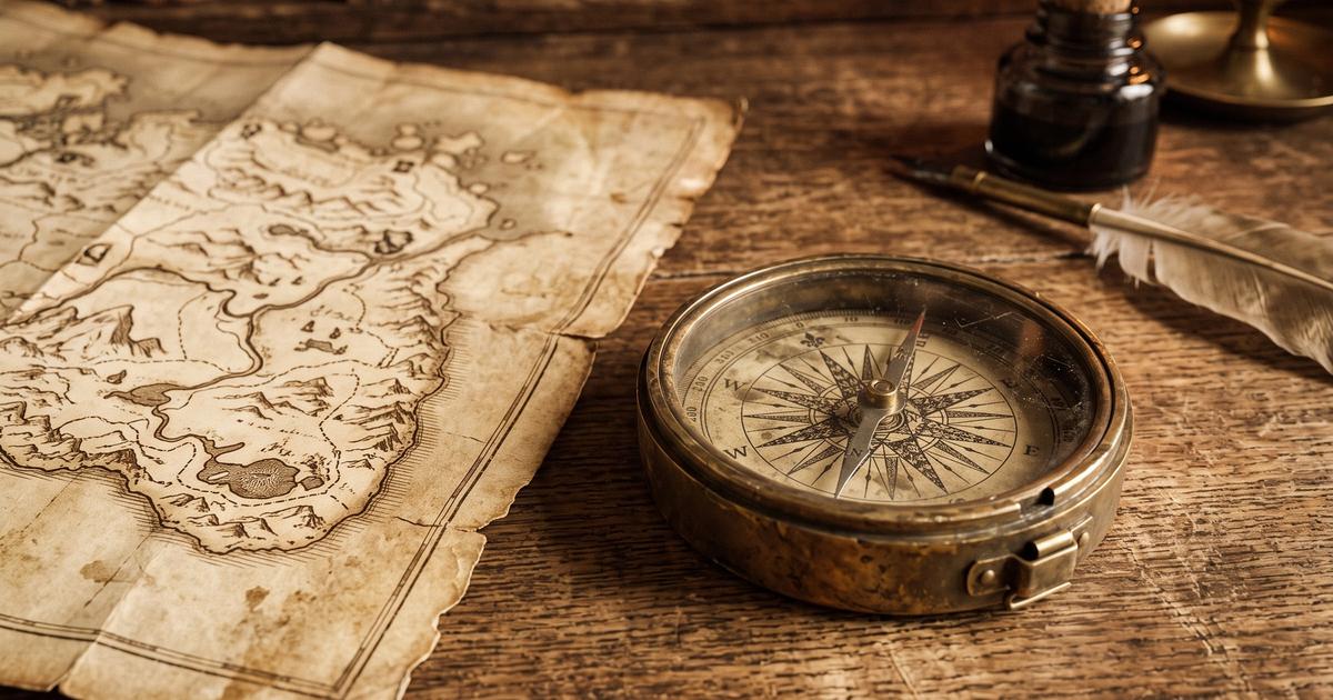 An antique compass and folded map on a wooden desk.