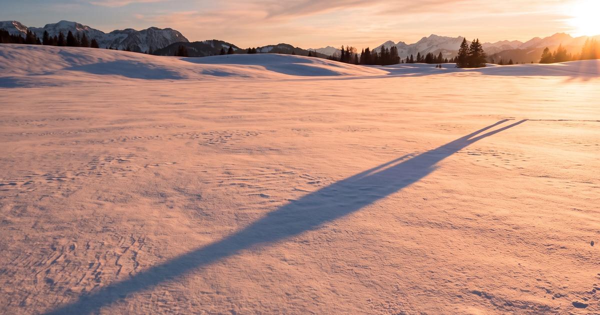 A long shadow stretching across snow with a soft blue tint in the light.