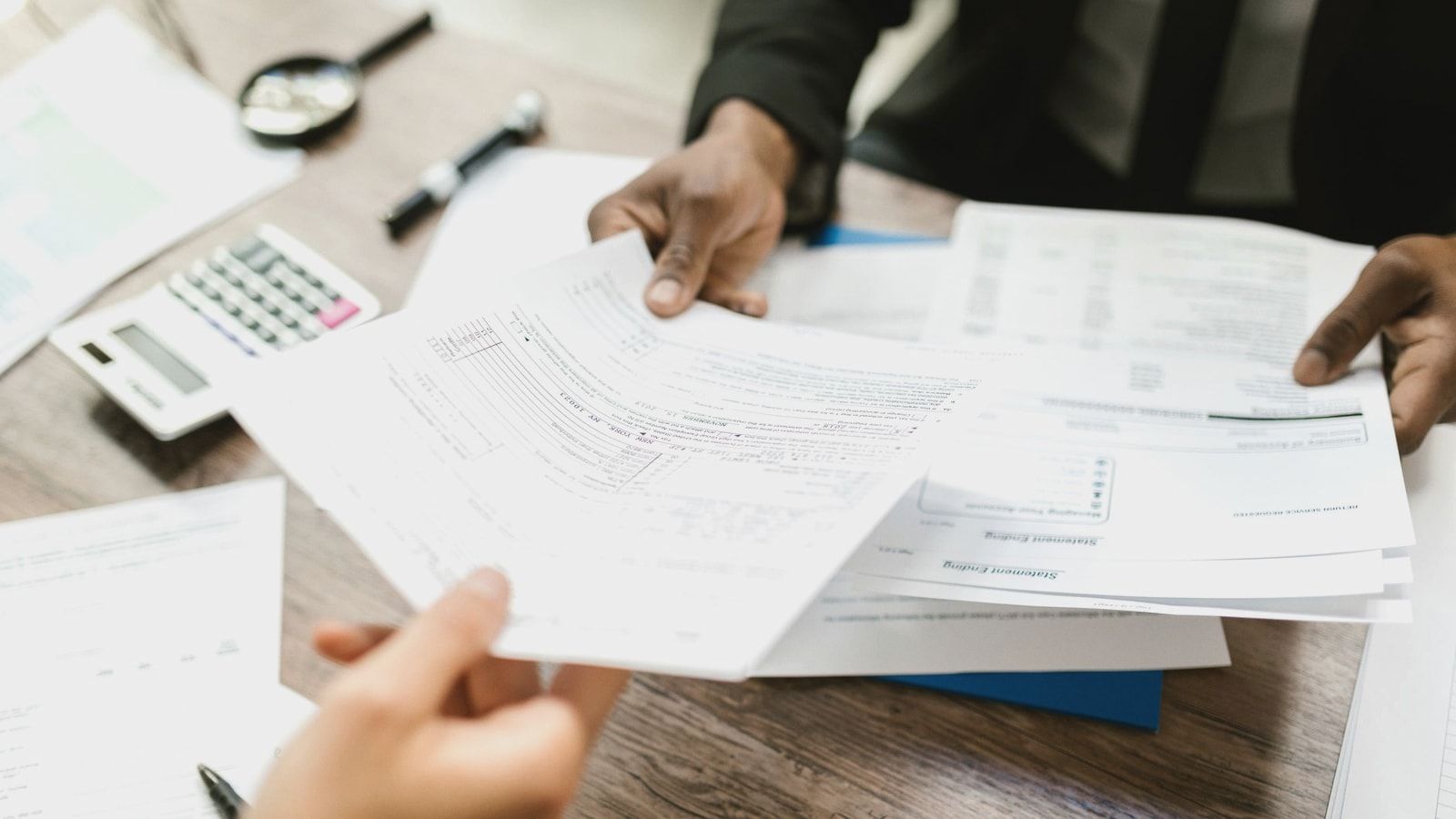Two professionals exchanging documents in an office setting, focusing on paperwork and data analysis.