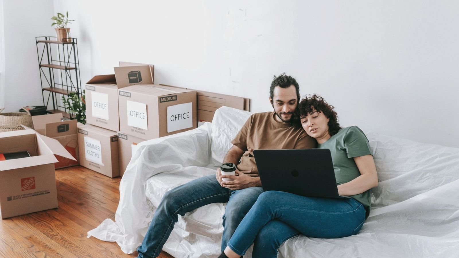 A couple sits together on a couch, using a laptop amidst moving boxes, enjoying relaxed time indoors.