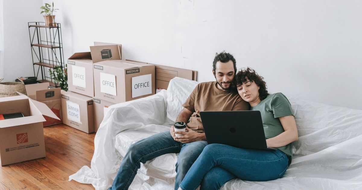 A couple sits together on a couch, using a laptop amidst moving boxes, enjoying relaxed time indoors.