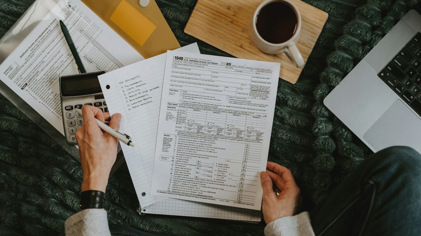 Person reviewing documents with calculator and laptop.