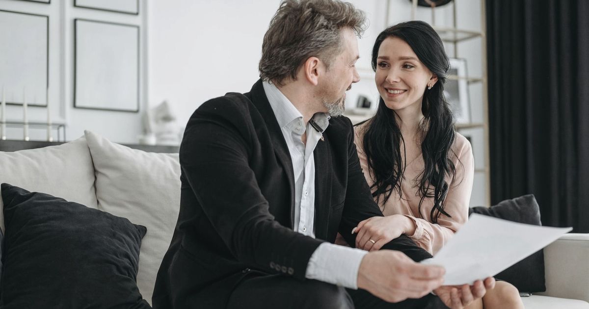 Couple smiling while sitting on a couch reviewing documents indoors.