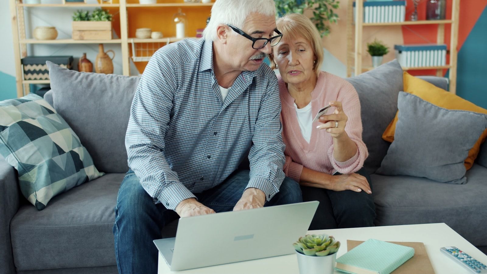 senior man and woman making electronic online payment with bank card using laptop at home. Money, retirement and shopping concept.