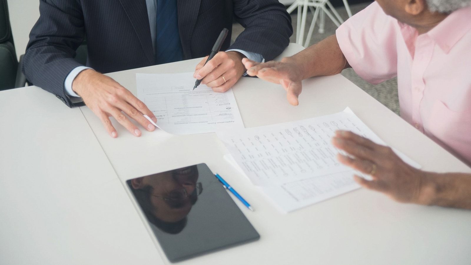 A business meeting between an elderly client and a consultant discussing documents at an office table.