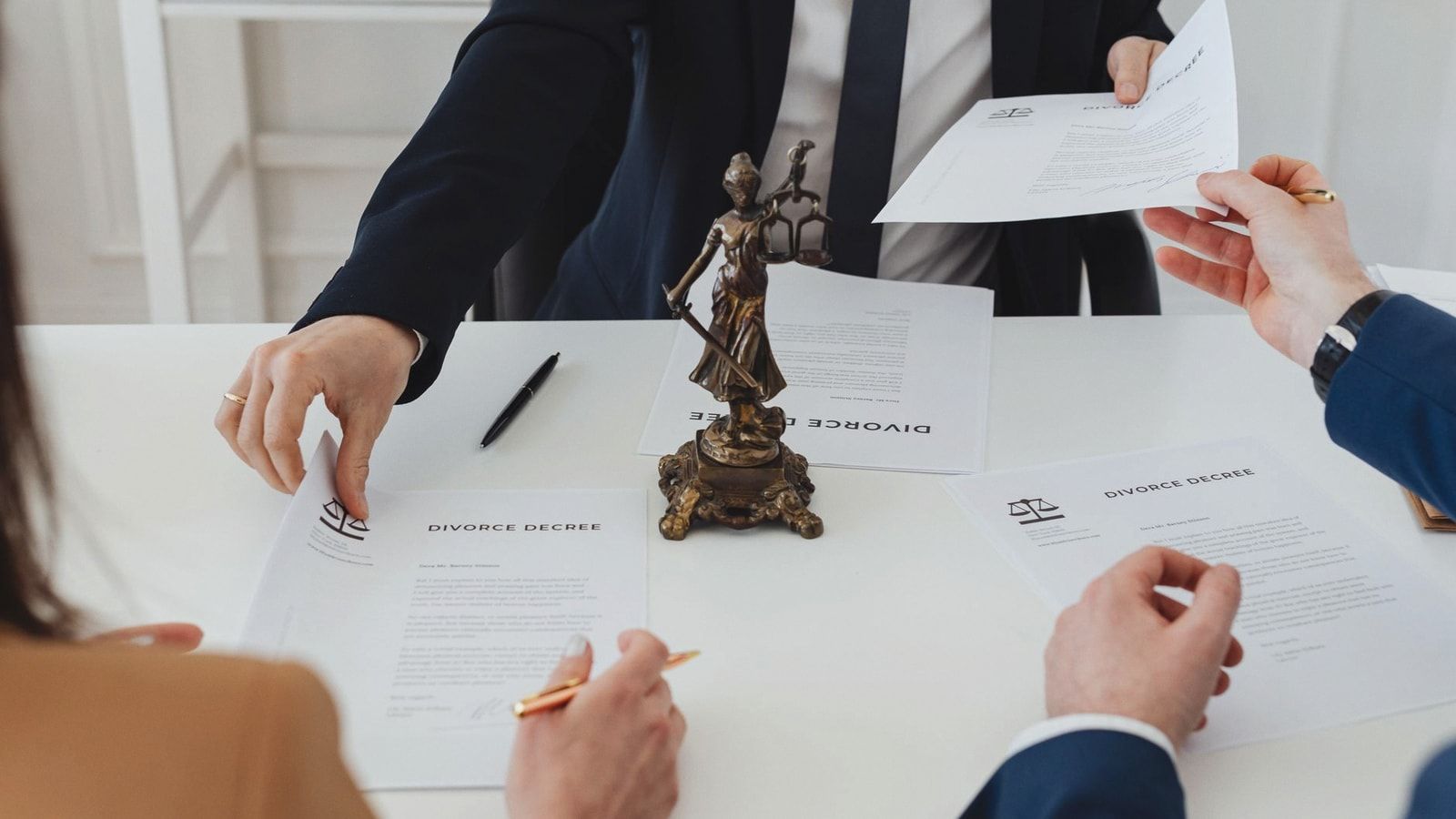 Three adults discussing divorce documents in a formal office setting with legal statue in view.