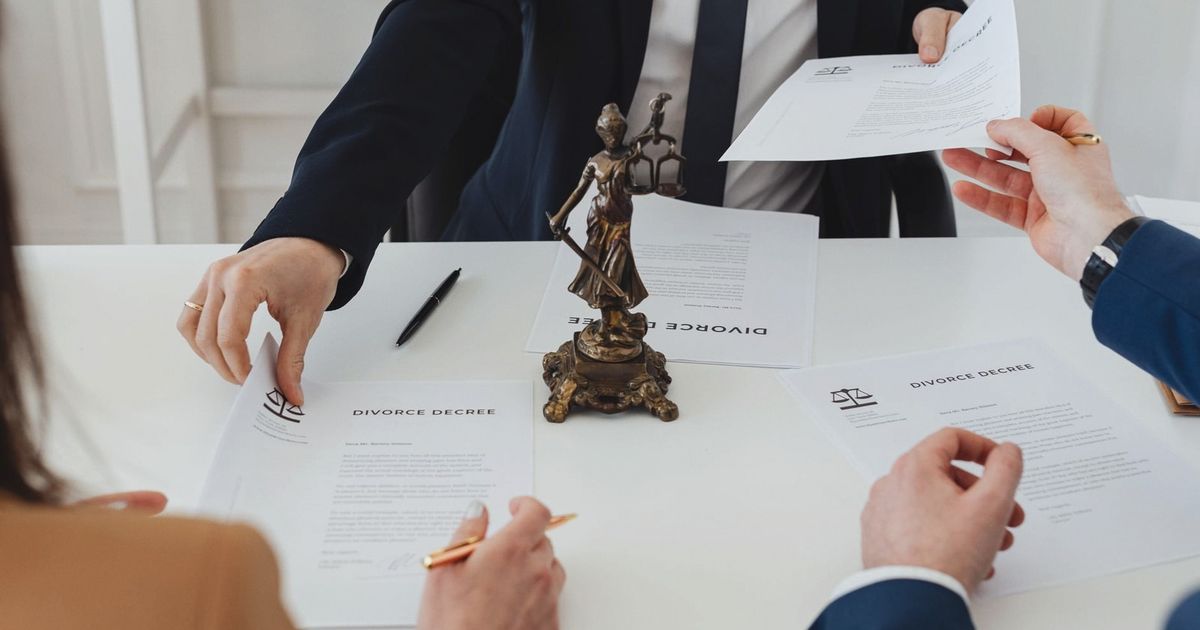 Three adults discussing divorce documents in a formal office setting with legal statue in view.