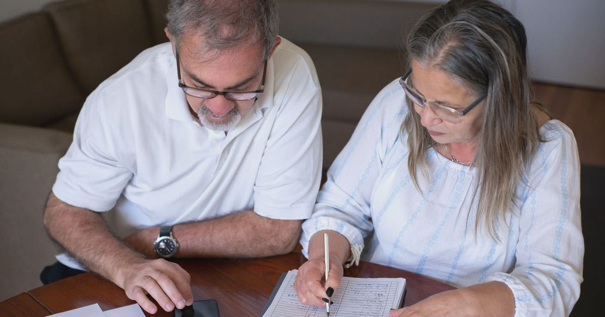 Elderly couple reviewing documents, using smartphone for online banking at home.