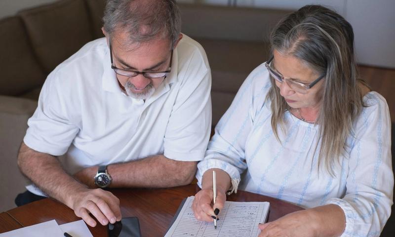 Elderly couple reviewing documents, using smartphone for online banking at home.