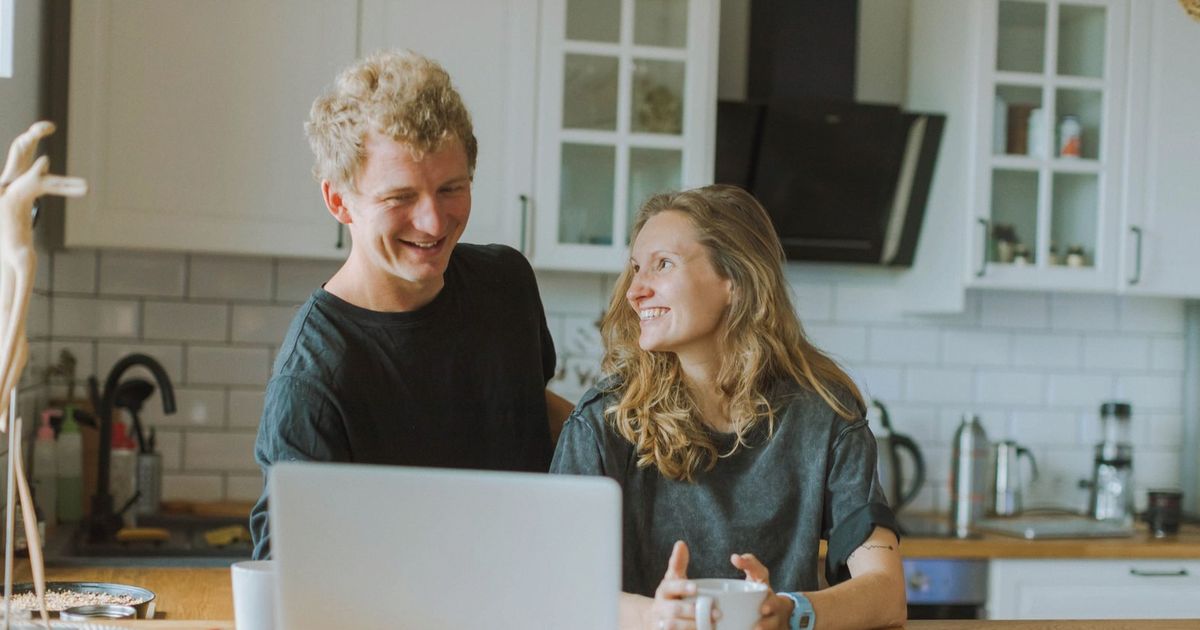 A cheerful couple shares a coffee and laughter in their modern kitchen, creating a cozy atmosphere.