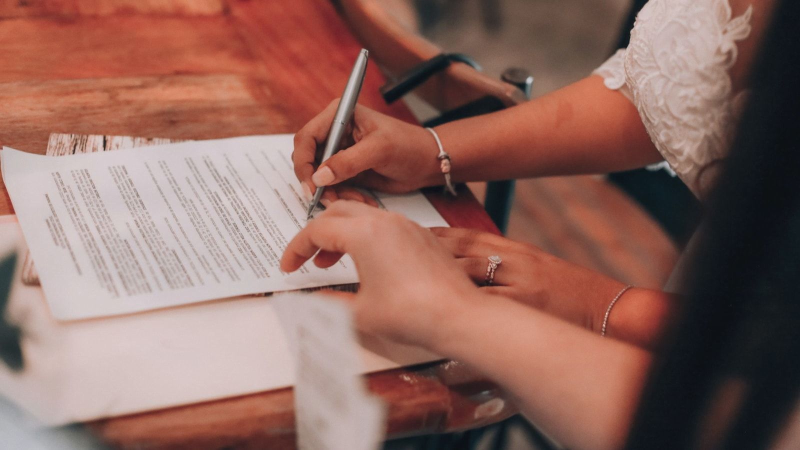 Hands signing an important document at a wooden table, symbolizing agreement and commitment.
