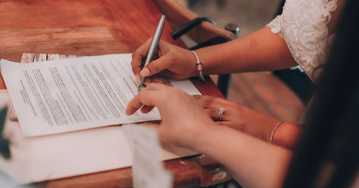 Hands signing an important document at a wooden table, symbolizing agreement and commitment.