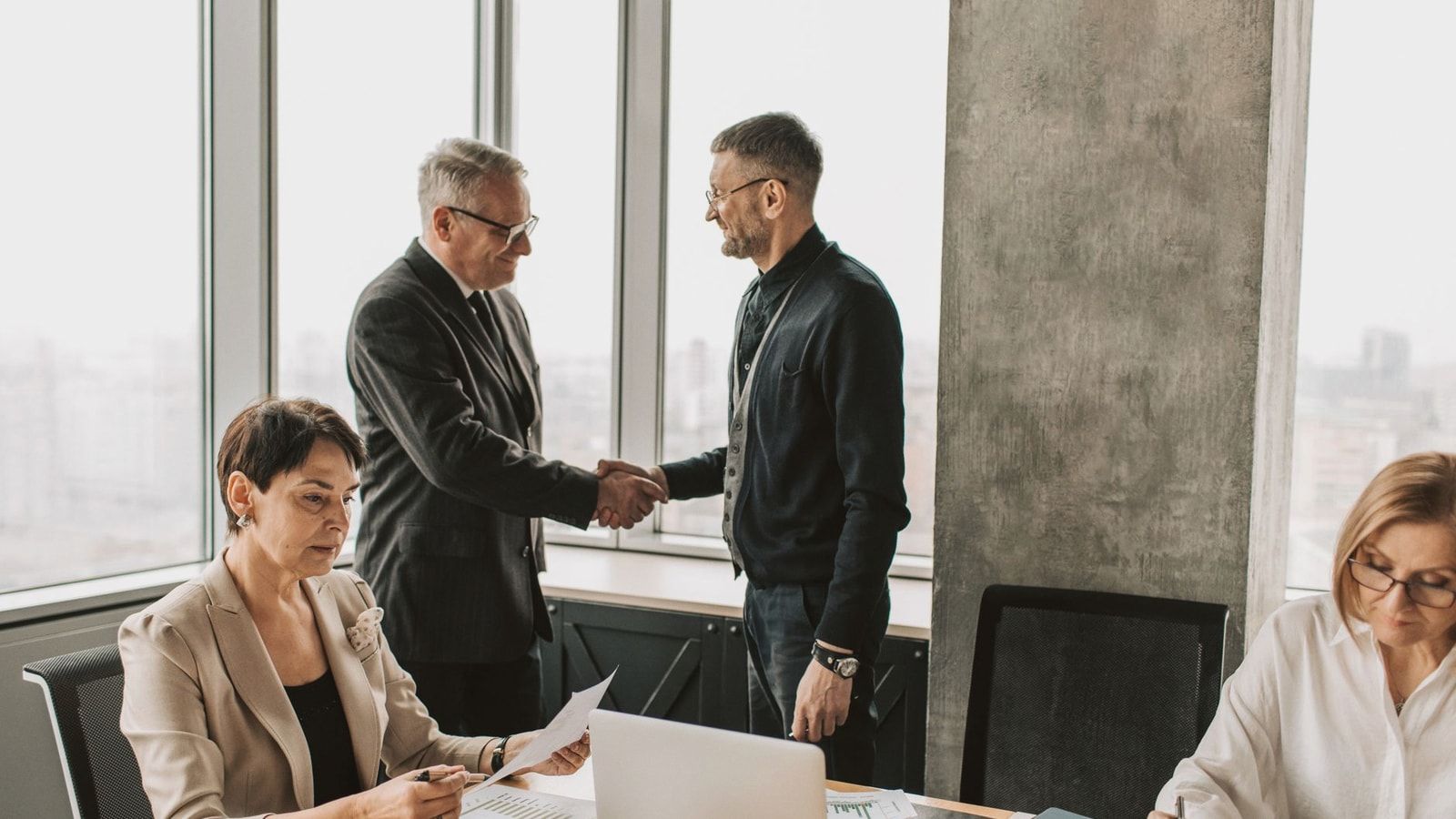 Professional business meeting with handshake in modern office room with multiple colleagues.