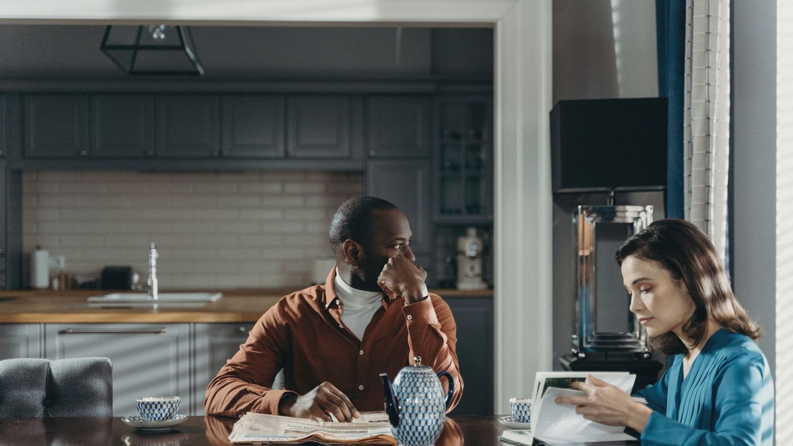 A couple sits at a dining table in a modern kitchen, reading and relaxing.