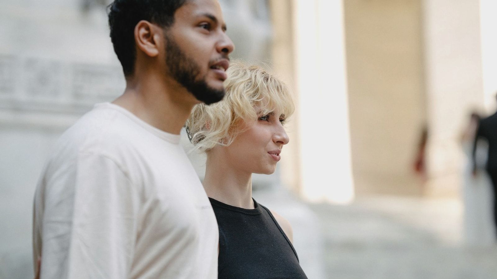A diverse couple walking together, exploring an urban architectural setting with bright natural lighting.