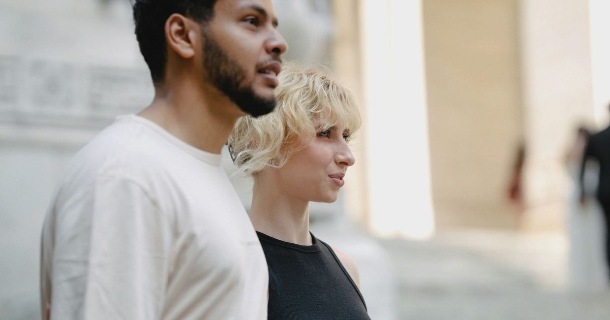 A diverse couple walking together, exploring an urban architectural setting with bright natural lighting.