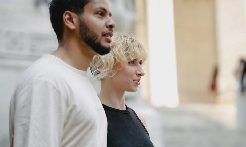 A diverse couple walking together, exploring an urban architectural setting with bright natural lighting.