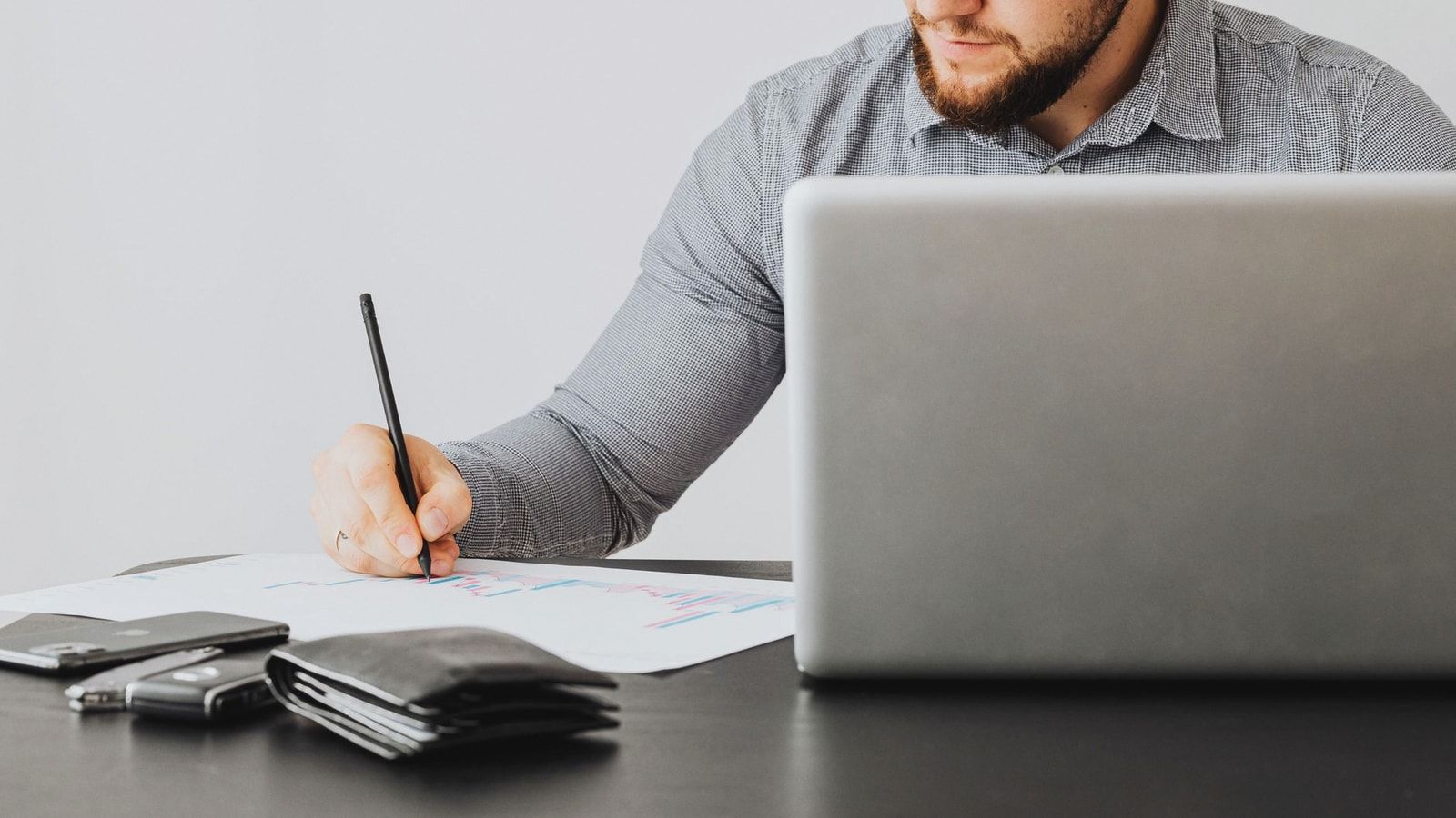 A focused man analyzing financial papers with a laptop in an office setting.