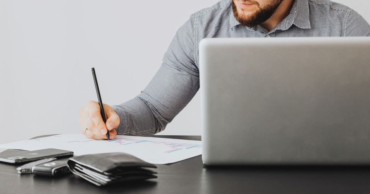 A focused man analyzing financial papers with a laptop in an office setting.