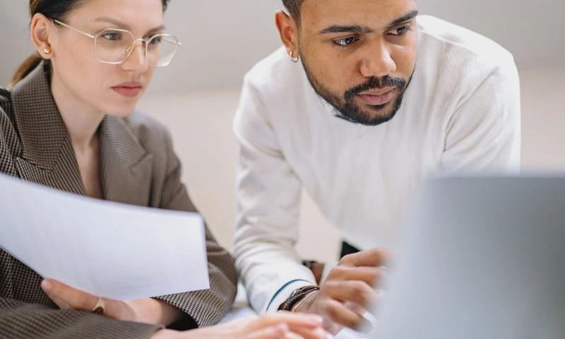 Two colleagues engaged in teamwork, analyzing documents in a modern office environment.