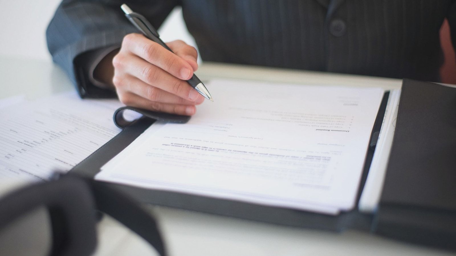 Close-up of a hand signing documents with a pen, symbolizing an important business contract.