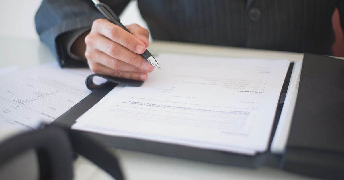 Close-up of a hand signing documents with a pen, symbolizing an important business contract.