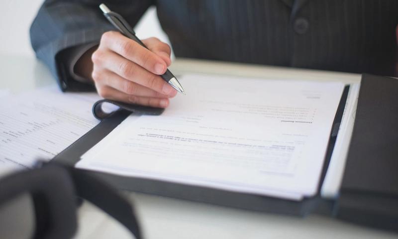 Close-up of a hand signing documents with a pen, symbolizing an important business contract.