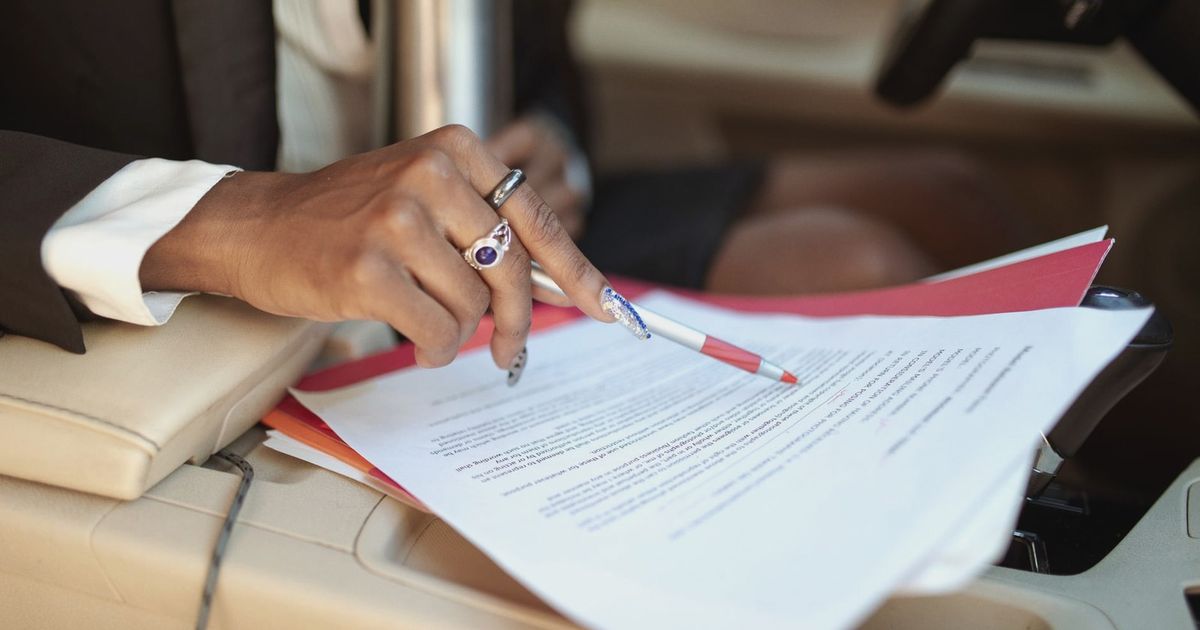 A professional reviewing documents in a car interior, focusing on hand and paperwork.