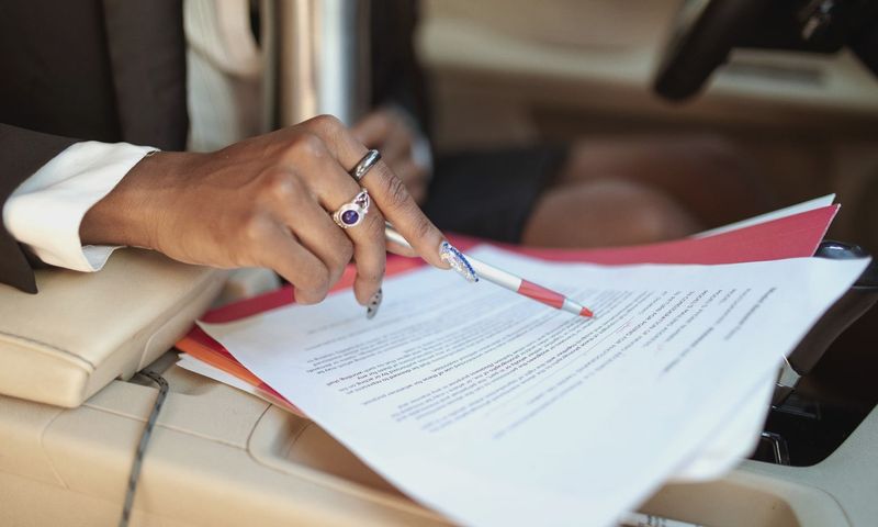 A professional reviewing documents in a car interior, focusing on hand and paperwork.