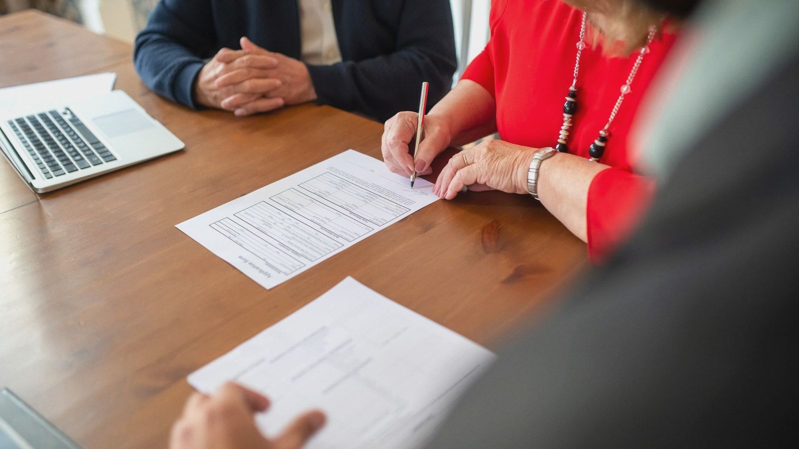 Two adults sign documents on a wooden table at a business meeting, emphasizing teamwork.